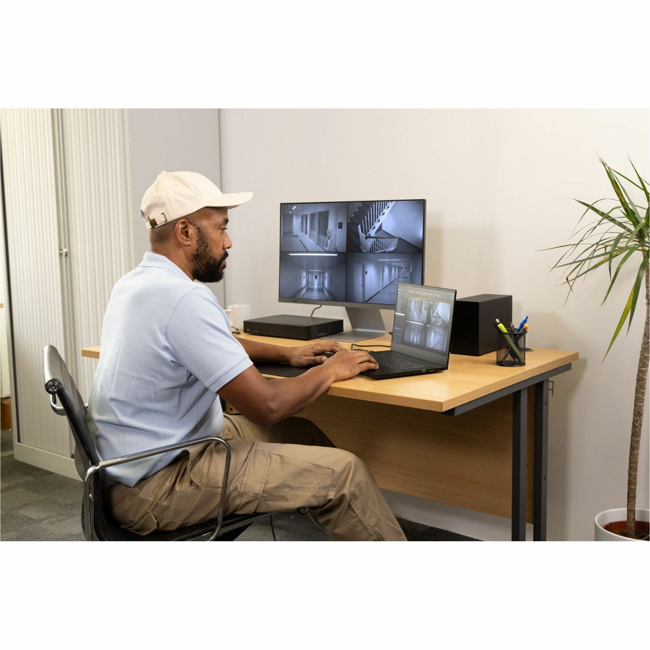 Security professional monitoring multiple surveillance camera feeds on desktop and laptop screens in control room setting